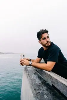 Middle age man posing with drink and black t-shirt resting on the pier