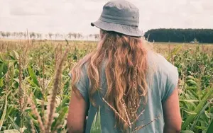 Light-haired woman walking on the farmland with a light-blue t-shirt and hat