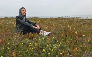 A smiling woman sitting on the grassy mountain top looking at the sky